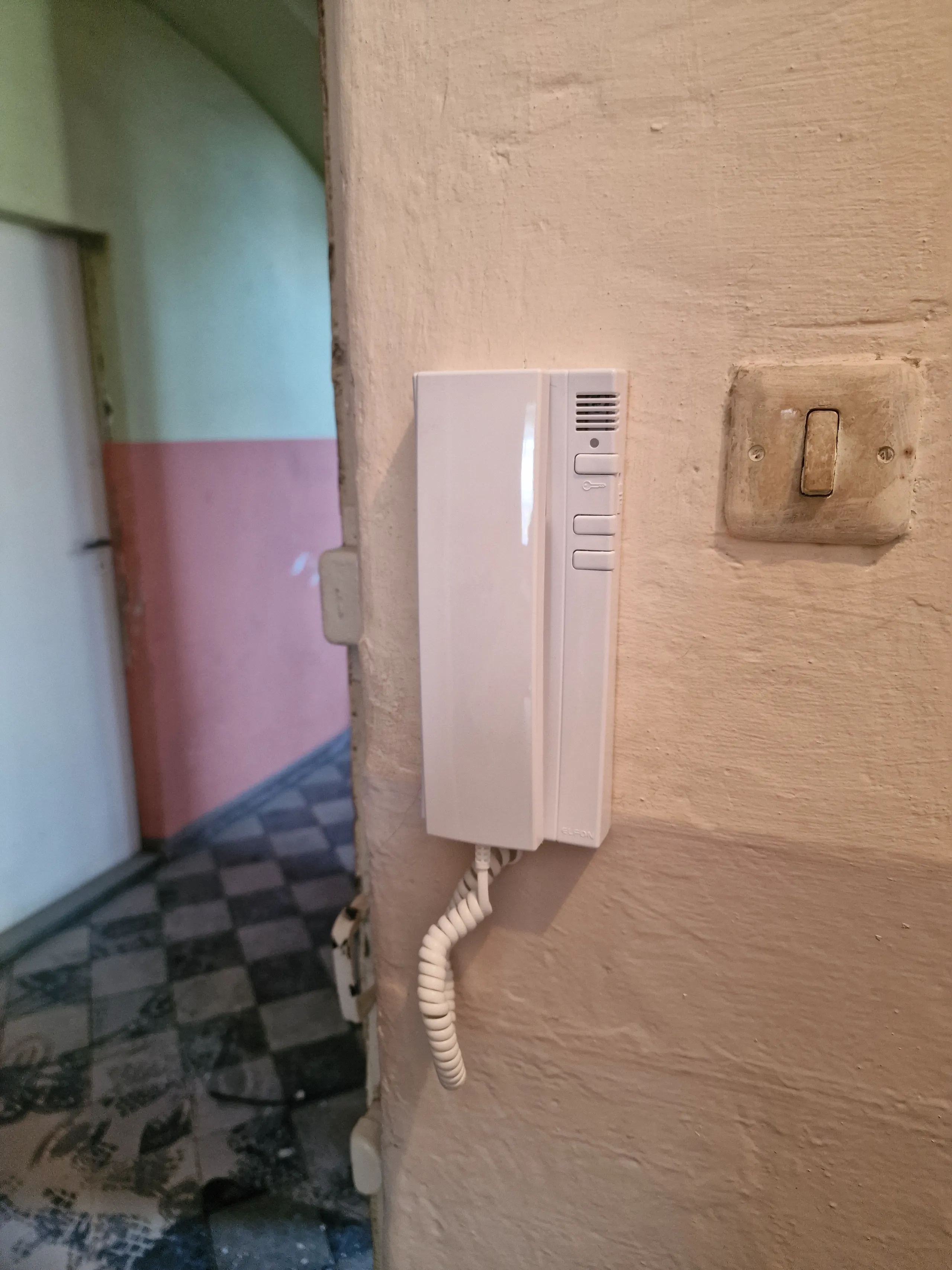 Wideodomofon zamontowany na ścianie, obok włączników, w korytarzu budynku