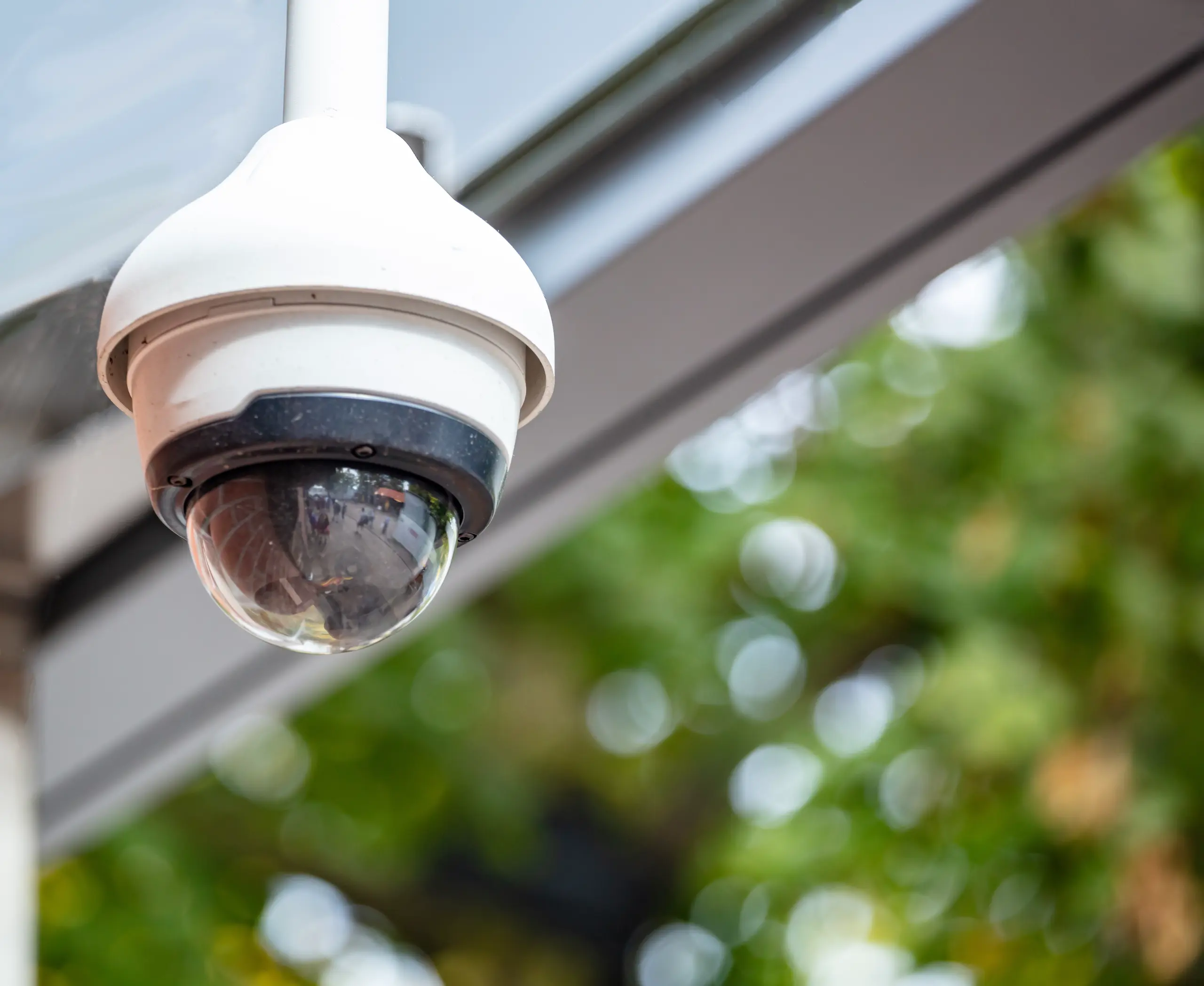 Kamera monitorująca zamontowana na zewnątrz budynku, w tle widoczne zielone liście