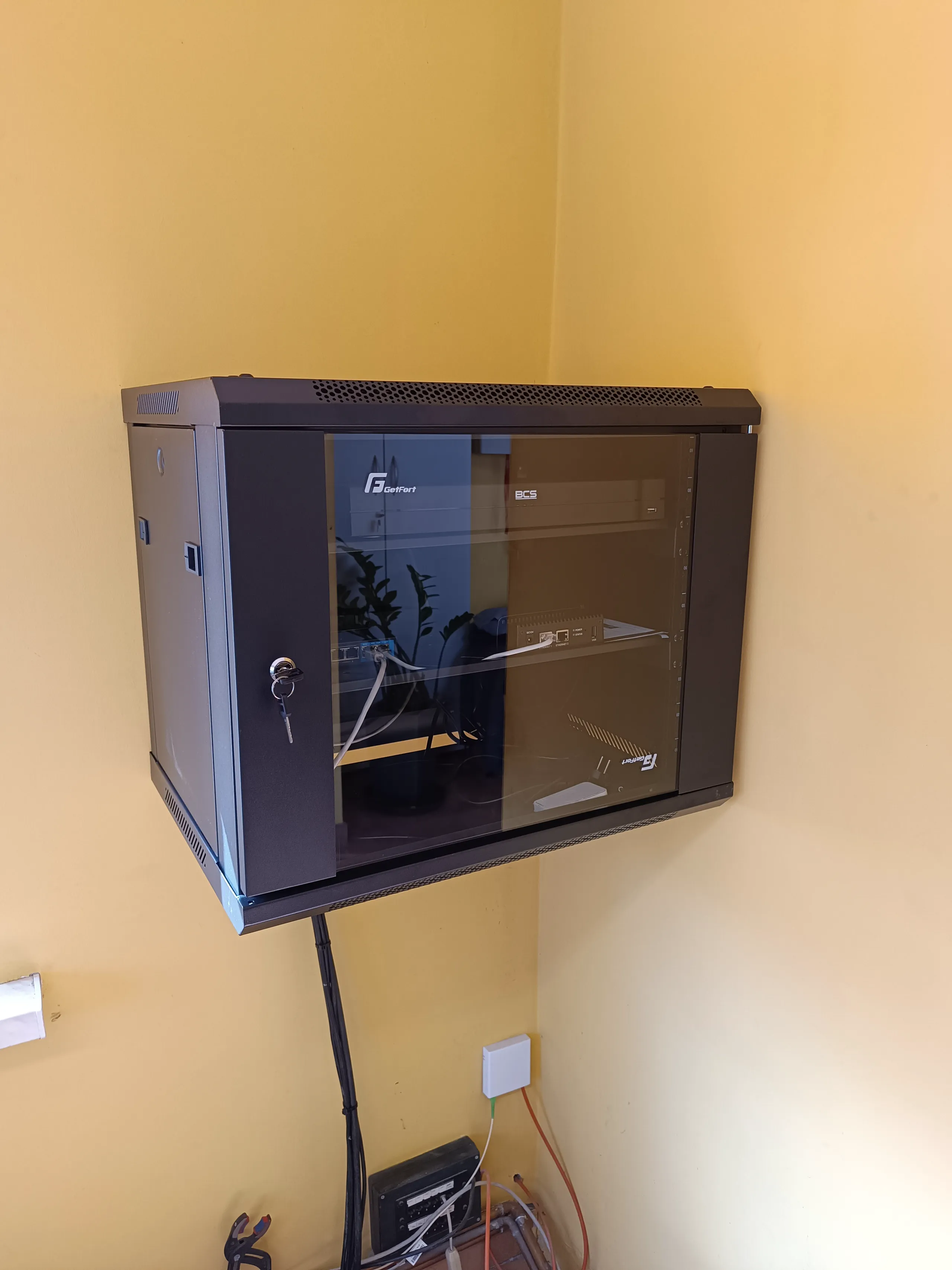 Szafka serwisowa zamontowana na ścianie, zawierająca sprzęt do instalacji sieci LAN oraz okablowania strukturalnego