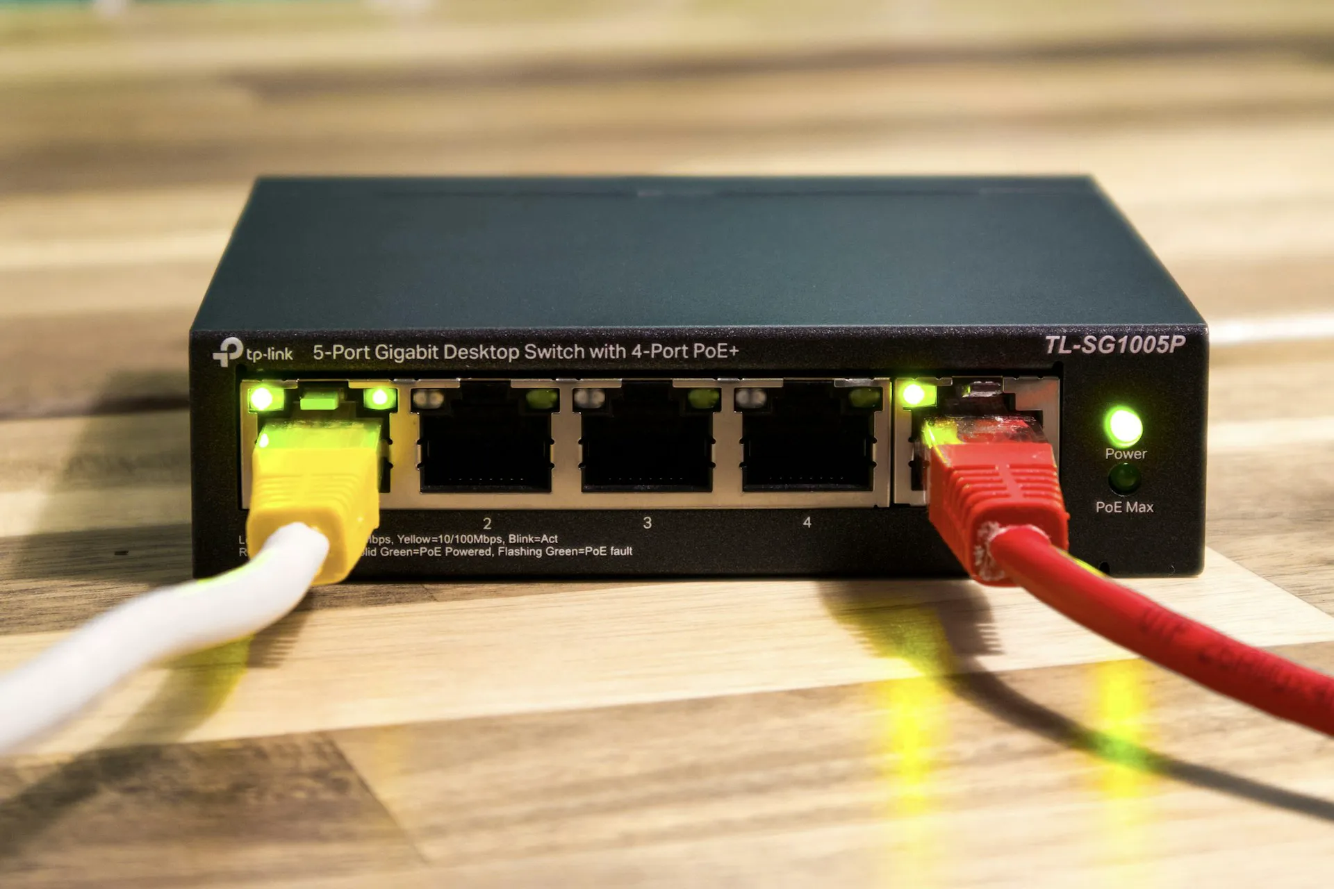 Przełącznik sieciowy z portami Ethernet, zasilany poprzez PoE, na tle drewnianego blatu