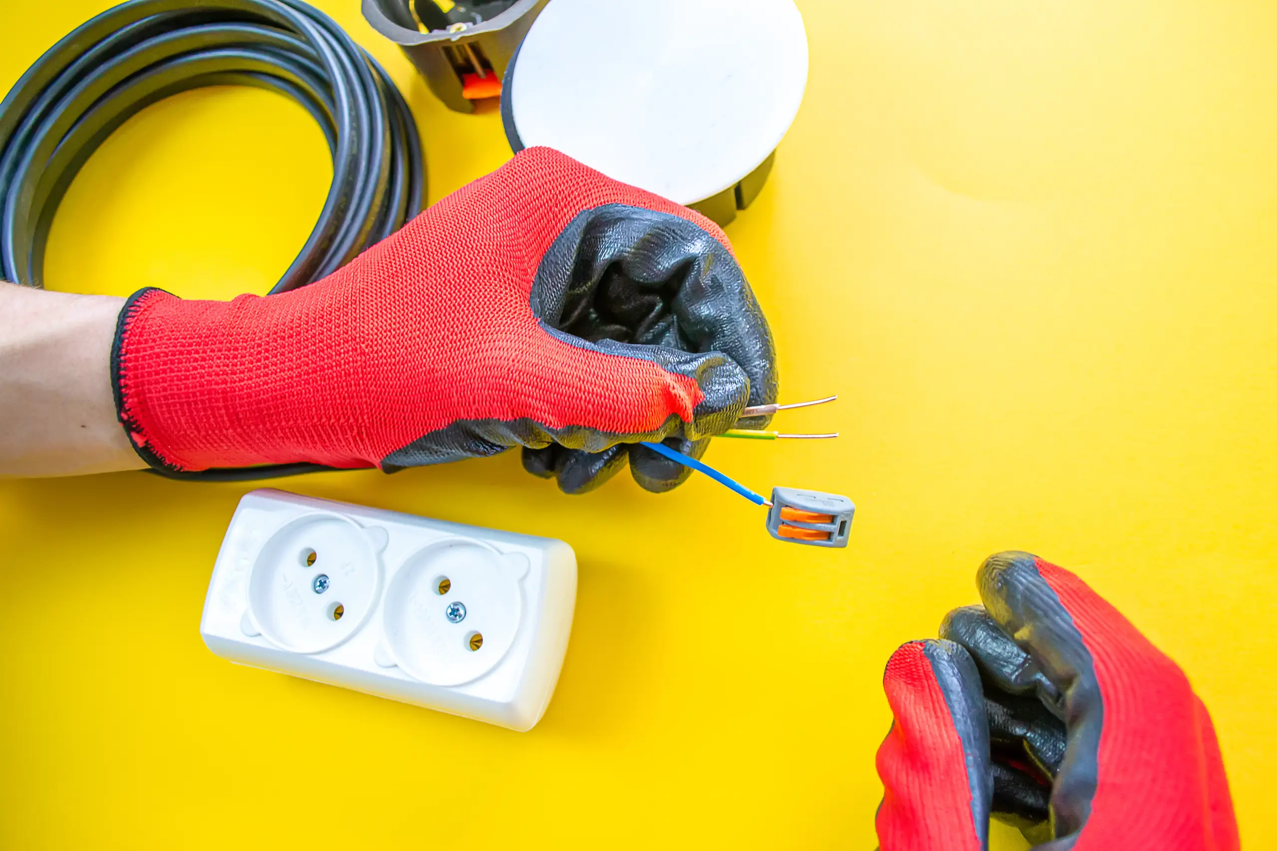 Pracownik instalujący gniazdko elektryczne, trzyma przewody i narzędzia w rękach