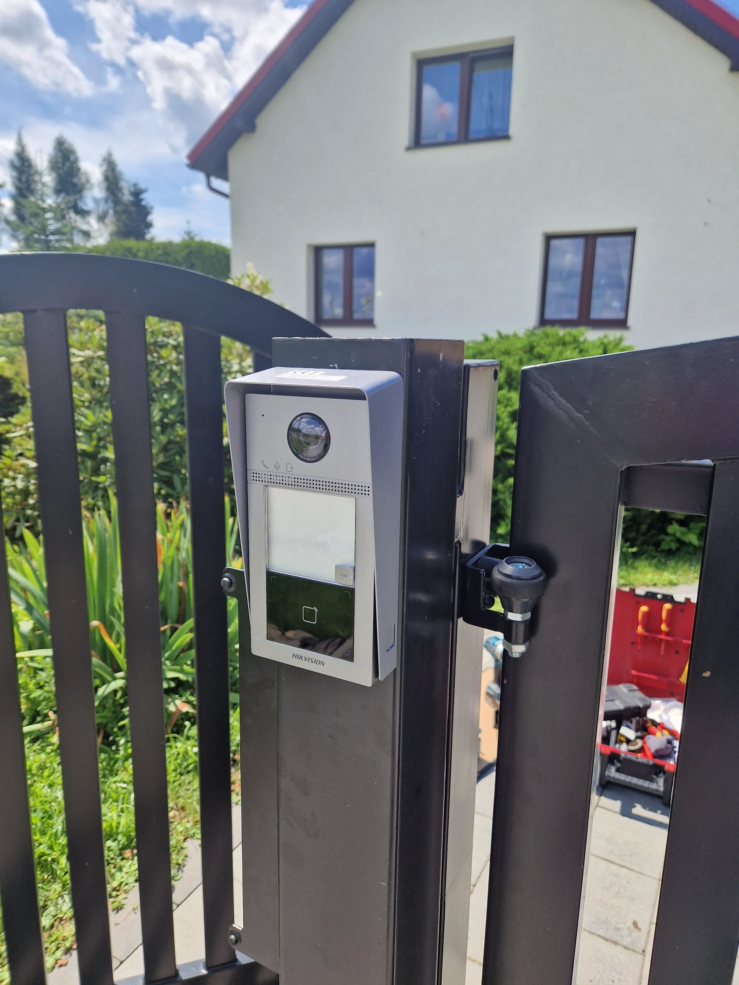 Wideodomofon zamontowany na furtce, obok zieleni i budynku mieszkalnego